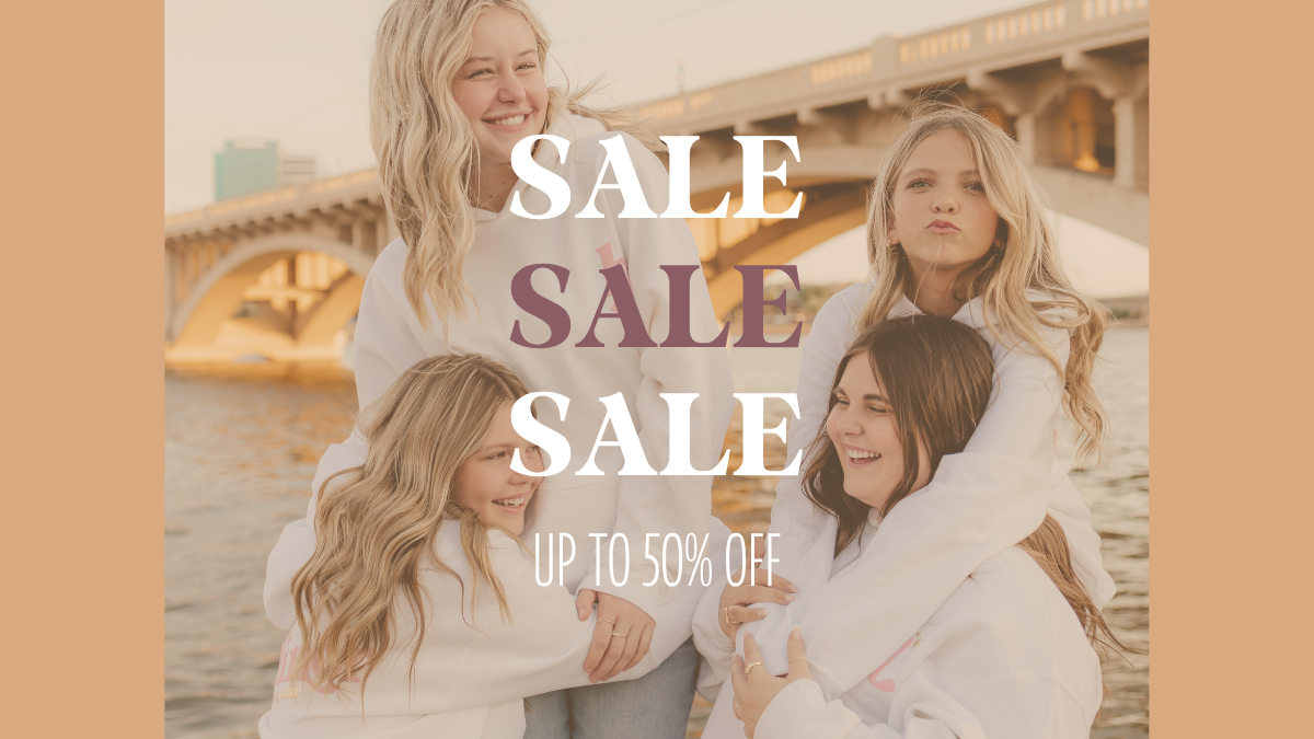 Four young women in matching white hoodies pose together outdoors in front of a bridge over water, with large overlaid text reading 'SALE SALE SALE' and smaller text 'UP TO 50% OFF'.