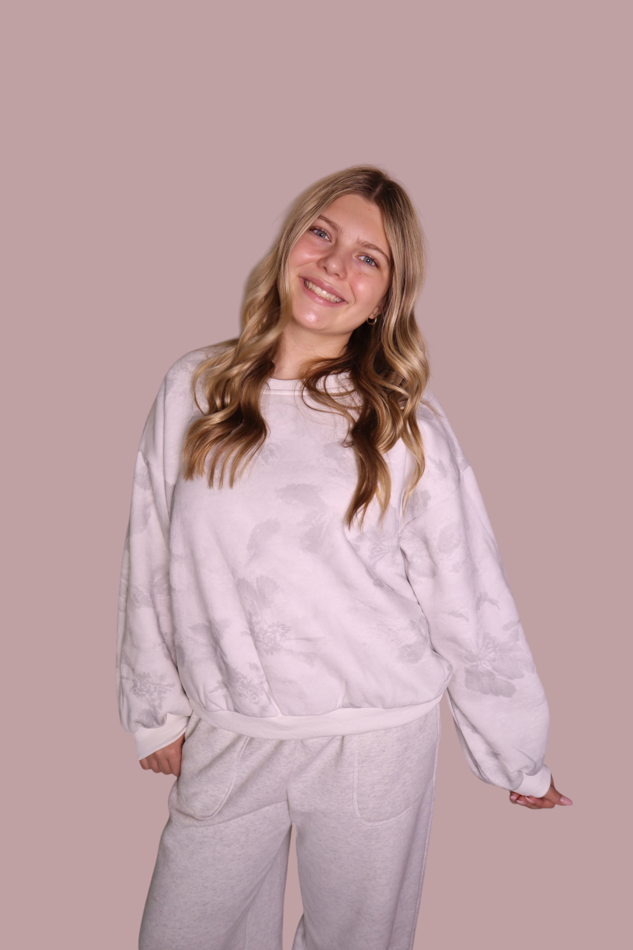 Woman wearing a light gray sweatshirt and pants against a beige background