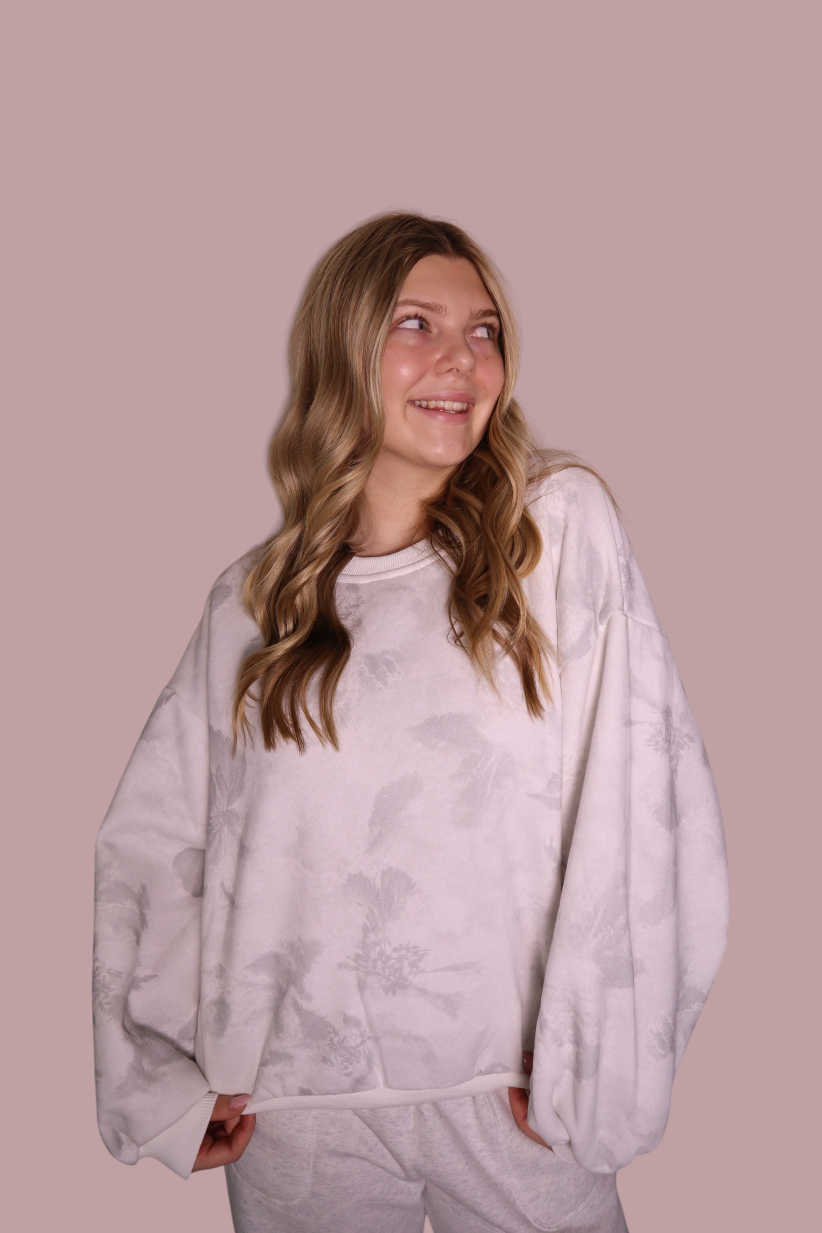 Person wearing a light gray tie-dye sweatshirt against a pink background